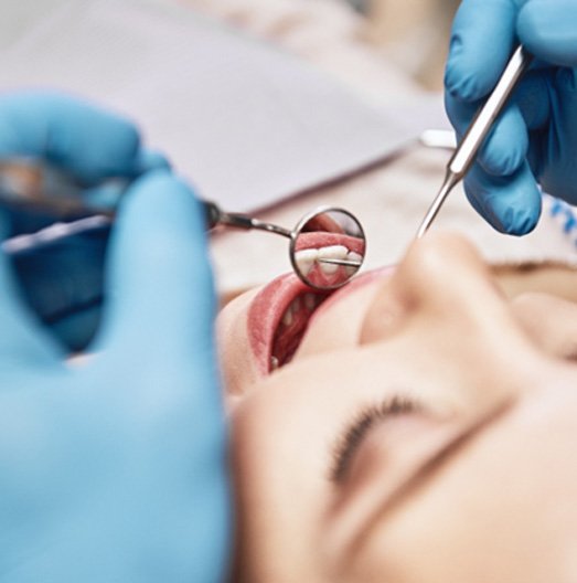 Dentist with blue gloves using dental instruments to examine teeth