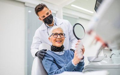 Dentist looking over a patient’s shoulder as she admires her new smile