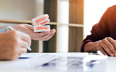 Dentist and patient discussing treatment with model teeth and X-rays