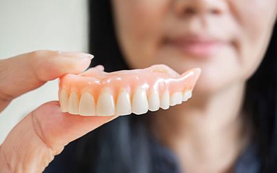 Woman blurry in background holding upper arch of dentures to foreground