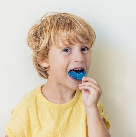 Young boy placing blue athletic mouthguard in his mouth