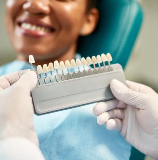 Closeup of cosmetic dentist selecting shade of veneer for smiling patient