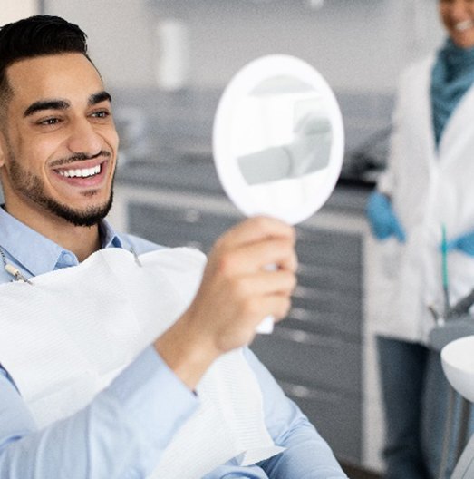 Man smiling at reflection in handheld mirror