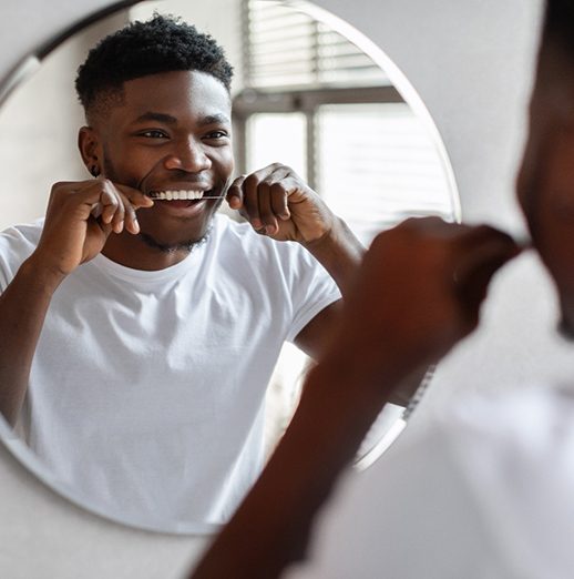 Man smiling while flossing teeth at restaurant