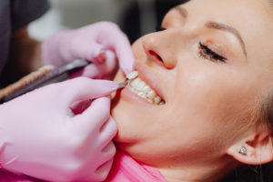 Dentist holding veneer by woman’s tooth