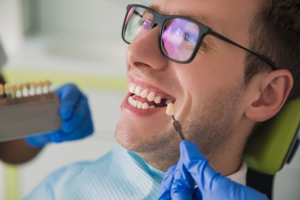 Man in glasses smiling as dentist holds sample tooth to gap in his smile