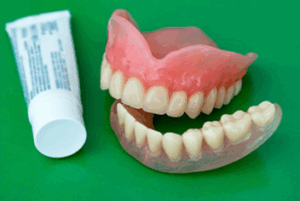A pair of dentures sitting next to denture adhesive