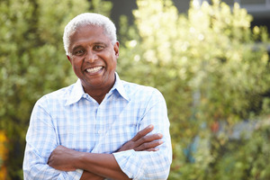 Senior man smiling outside with his arms folded