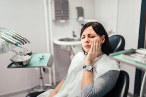 Woman in dentist's chair holding jaw in pain.