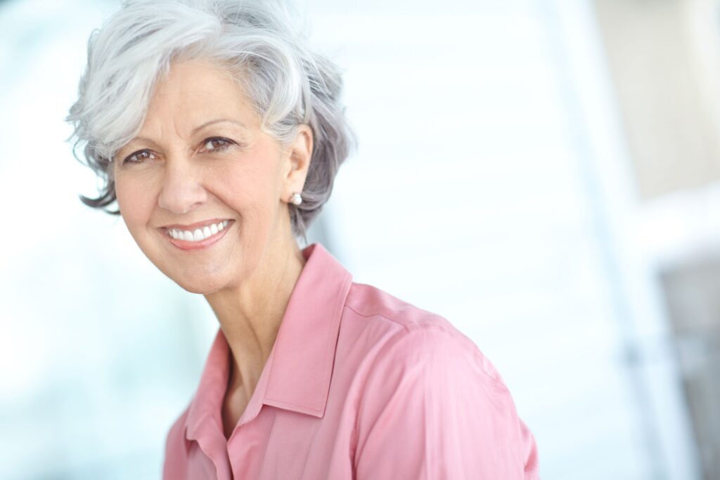 Woman in pink shirt with gray hair smiling with bright teeth