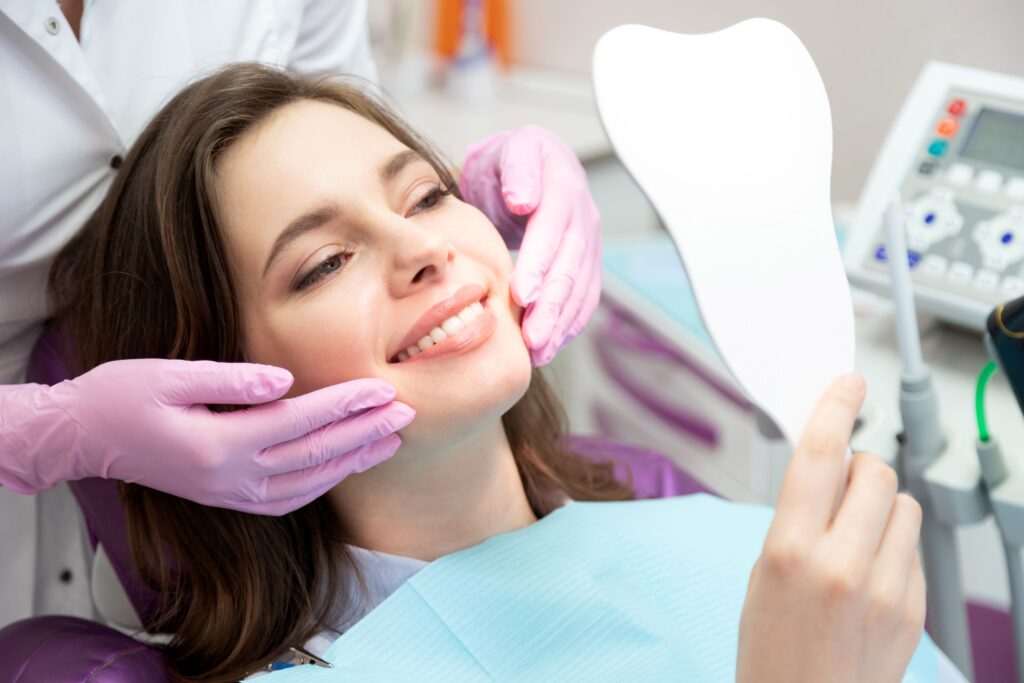 Woman in dental chair smiling at reflection with dentist touching her cheeks